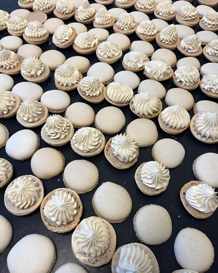 Tientallen macaronschelpen op een bakplaat, elk met een met de hand gespoten rozet