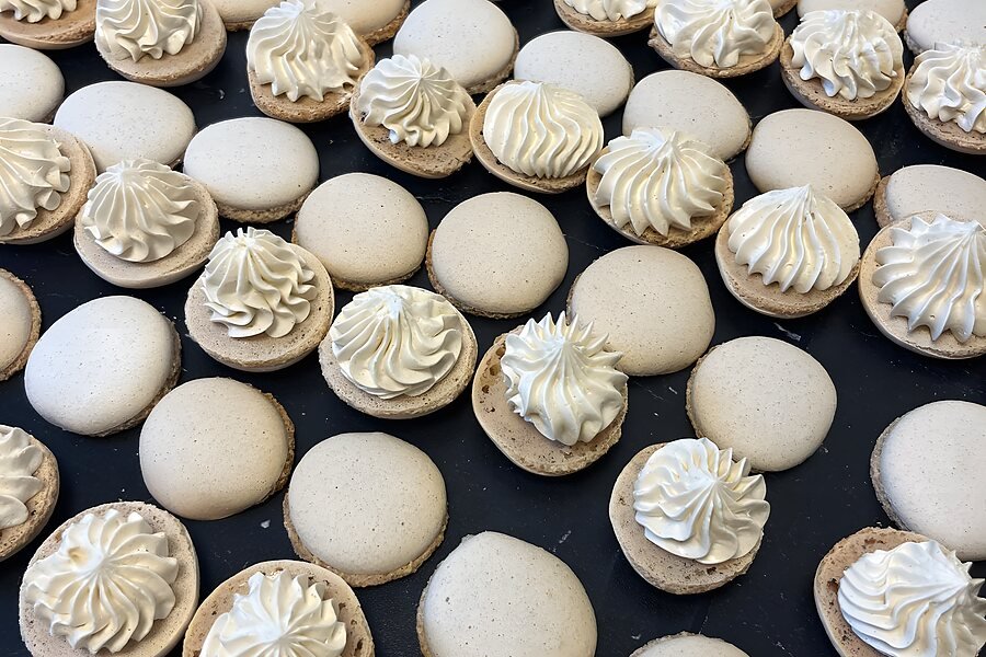 Een volle bakplaat macaronschelpen, elk met een met de hand gespoten rozet crème